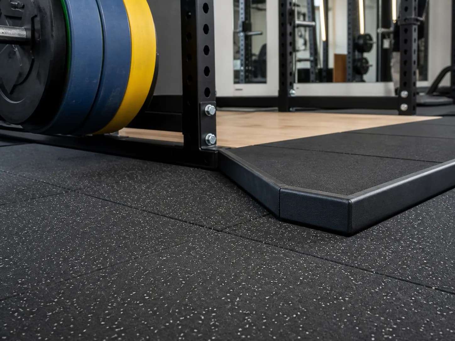 Heavy rubber tiles beside a lifting platform and squat rack
